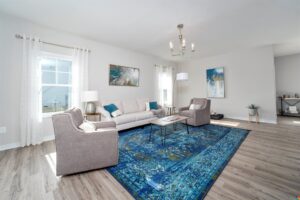 Modern living room in Lot 22 with a blue rug, gray sofas, white couch, abstract paintings, and chandelier.