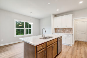Modern kitchen with island in Poplar Village, white cabinets, wood floors, and a large window letting in natural light.