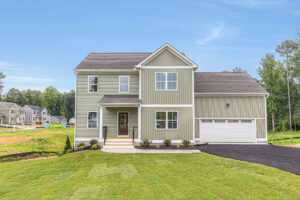 Light green two-story house with a garage in Poplar Village, Lot 22, featuring a porch and a well-kept lawn.