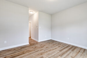 Empty room with light gray walls, wood flooring, and a hallway in Poplar Village Lot 22.