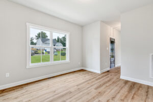 Bright, empty room in Poplar Village with light wood floors, white walls, and a large window overlooking a green yard.