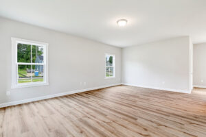 Empty room in Poplar Village, Lot 22, with light wood flooring, white walls, two windows, and a ceiling light fixture.