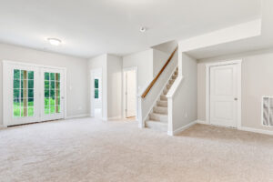 Bright, spacious room in Poplar Village with carpet, stairs, French doors, and two white doors against light walls.
