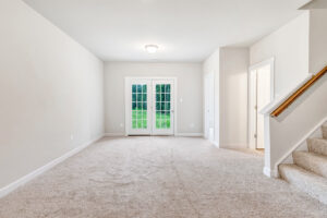 Bright, empty room with beige carpet, white walls, French doors, and a staircase on Lot 22 in Poplar Village.