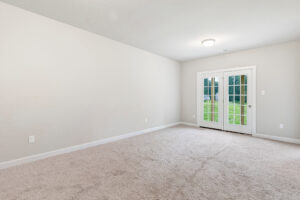 Empty carpeted room with beige walls, ceiling light, and double glass doors in Poplar Village Lot 22.