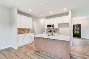 Modern kitchen in Poplar Village features white cabinets, center island, stainless appliances, and wood flooring.