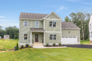 Charming two-story light green home in Poplar Village with a two-car garage, front porch, and landscaped yard.