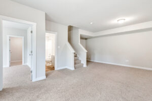 Bright, carpeted room in Poplar Villages Lot 22 with stairs, two doorways, bathroom, neutral walls, and ceiling light.