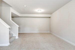 Empty carpeted room with beige walls, staircase on left, and ceiling light fixture in Poplar Village Lot 22.