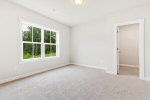 Empty, bright bedroom in Poplar Villages Lot 22 with beige carpet, white walls, and a large window.