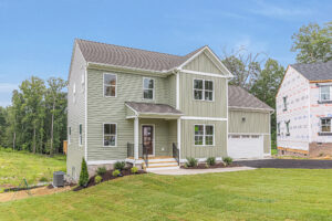 Two-story green house with white trim on Lot 22, Poplar Village, featuring a porch, garage, and lush trees.