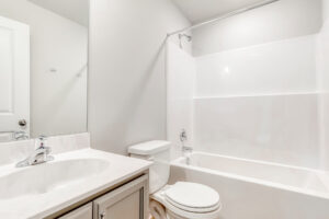 White bathroom in Poplar Villages Lot 22 with a sink, toilet, and bathtub against a light-colored wall.