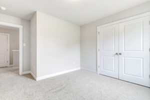 Empty room in Poplar Village with beige carpet, white walls, double closet doors. Door opens to hallway. Lot 22.