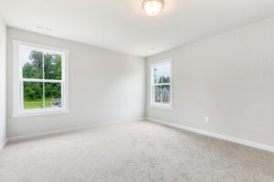 Empty, carpeted room with two windows in Poplar Villages Lot 22, featuring light gray walls and a ceiling light.