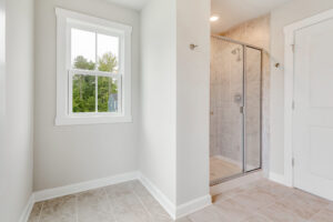 Bright bathroom in Lot 22, Poplar Village with tiled floor, glass shower, white walls, and a window showing greenery.