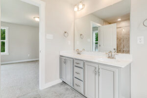 Modern bathroom in Poplar Village with double vanity, large mirror, and view into the carpeted bedroom.