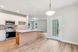 Bright modern kitchen in Poplar Village with island, white cabinets, stainless steel appliances, and glass door to outside.