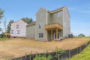Newly built three-story house with a deck and unfinished yard in Poplar Village, next to Lot 22 under construction.