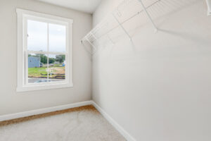 Empty walk-in closet with white wire shelf, beige carpet, and window overlooking Poplar Village in Lot 22.