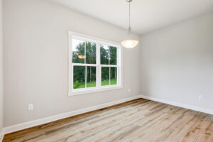 Bright, empty room with wood floors in Poplar Village Lot 22, light gray walls, large window, and ceiling light.