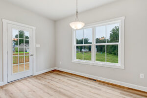 Bright empty room with hardwood floors in Poplar Village, window, deck door, and a hanging ceiling light.