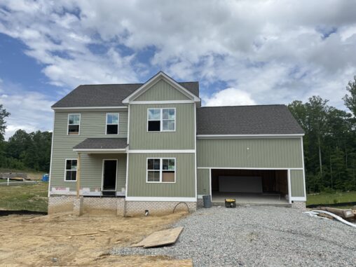 Two-story green house under construction on Lot 22, Poplar Village; garage, dirt, trees, and a cloudy sky above.