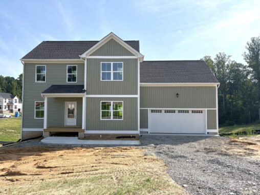 Lot 22, Poplar Village: Two-story gray house with white trim, double garage, and unfinished yard on a sunny day.
