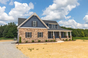 Two-story house with stone and blue siding, front porch, and gable roof on a large sandy lot.