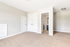 Bright, empty bedroom with beige carpet, white doors, and an open doorway leading to a bathroom.