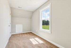 Small empty room with beige carpet, white walls, and a window showing a green field and blue sky outside.