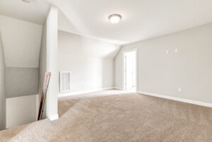 Empty carpeted room with white walls, ceiling light, and doorway leading to another room.