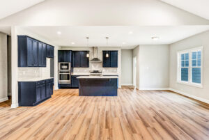 Modern kitchen with navy cabinets, island, stainless steel appliances, and wood flooring in an open room.