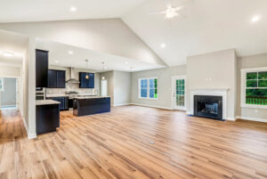 Open-concept living space with wood floors, modern kitchen, fireplace, large windows, and patio door.