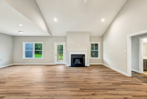 Spacious living room with wood floors, a white fireplace, and large windows letting in natural light.