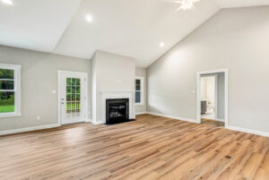 Spacious, empty living room with wood floors, fireplace, large windows, and a door to the outside.