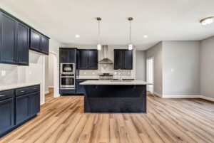 Modern kitchen with dark cabinets, island, pendant lights, stainless appliances, and light wood flooring.