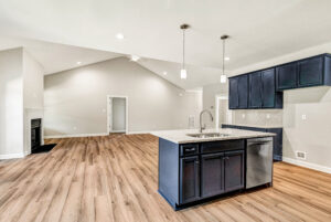 Modern open kitchen with navy cabinets, island, stainless appliances, and wood flooring in spacious living area.