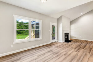 Bright living room with wood floors, large window, glass door, and a fireplace on a white wall.