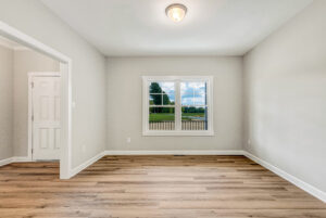 Empty room with light-colored walls, wood flooring, and a window showing a green outdoor view.