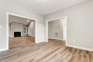 Bright, empty room with light wood floors, beige walls, and wide doorways leading to other rooms.