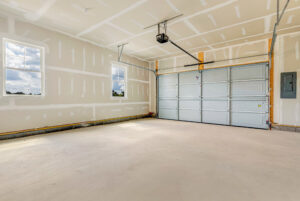 Empty two-car garage with unfinished drywall, two windows, and a closed garage door.