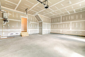 Empty, newly constructed garage with unfinished drywall, concrete floor, and a door with wooden steps.