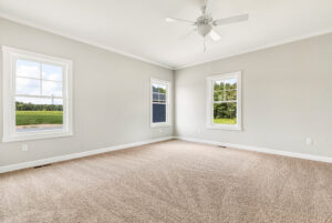Empty room with beige carpet, light gray walls, three windows, and a ceiling fan.