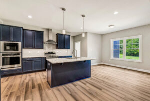 Modern kitchen with navy cabinets, island, stainless appliances, wood flooring, and large window.