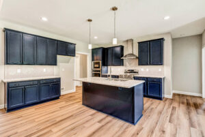 Modern kitchen with navy cabinets, granite island, stainless appliances, and wood-style flooring.
