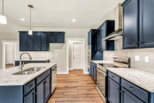 Modern kitchen with navy cabinets, granite countertops, stainless steel appliances, and wood flooring.