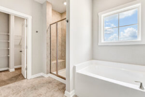 Bright bathroom with a large bathtub, glass shower, walk-in closet, and a window letting in natural light.