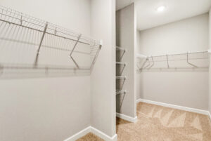 Empty walk-in closet with white wire shelving on beige carpet and light-colored walls.