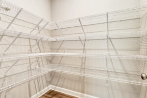 Empty walk-in pantry with white wire shelving on beige walls and wood floor.