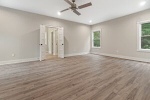 Spacious empty room with wood flooring in one of the elegant new homes in Richmond VA, featuring beige walls and double doors.